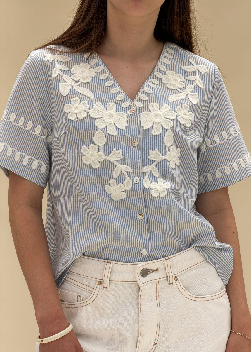 Blouse femme en coton rayé bleu et blanc à broderies fleuries blanches sur le buste, col V boutonné nacre, manches courtes, portée de face, esprit côtier Le Touquet-Paris-Plage Dune & Coton — Couleur: Bleu ciel