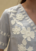 Détail des broderies florales blanches en relief sur une blouse en coton rayé bleu femme, gros plan sur le travail de fleurs et feuillages, Dune & Coton — Couleur: Bleu ciel