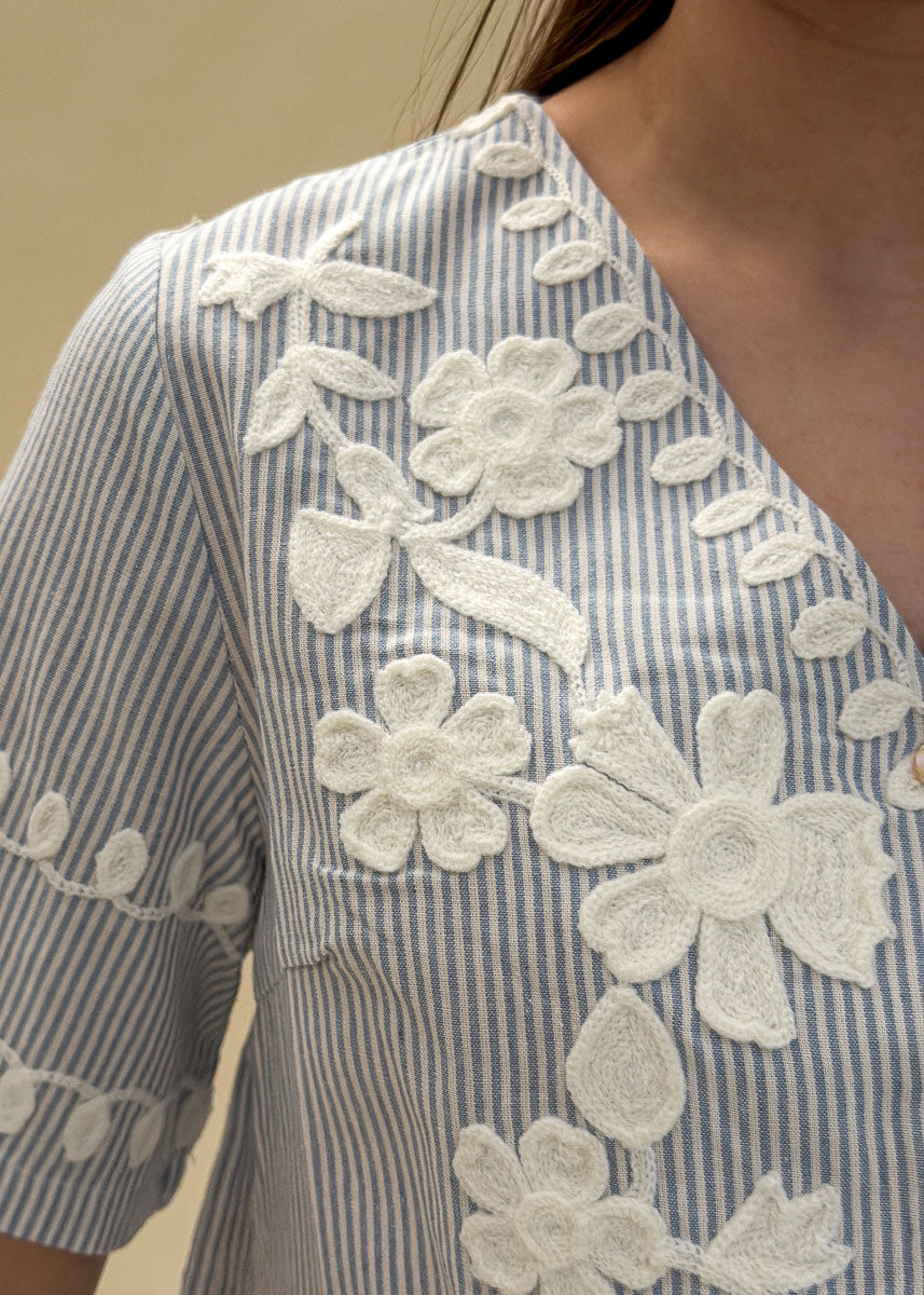 Détail des broderies florales blanches en relief sur une blouse en coton rayé bleu femme, gros plan sur le travail de fleurs et feuillages, Dune & Coton — Couleur: Bleu ciel
