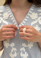 Détail du col V boutonné nacre et des broderies fleuries d'une blouse en coton rayé bleu femme, gros plan sur l'encolure, Dune & Coton — Couleur: Bleu ciel