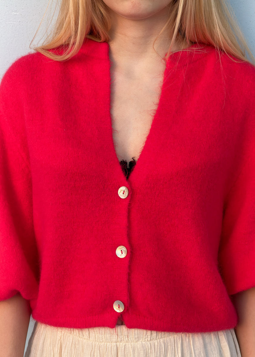 Gros plan sur les boutons nacrés et le col en V d'un gilet en maille rouge femme, coupe courte, Dune & Coton — Couleur: Rouge Cerise